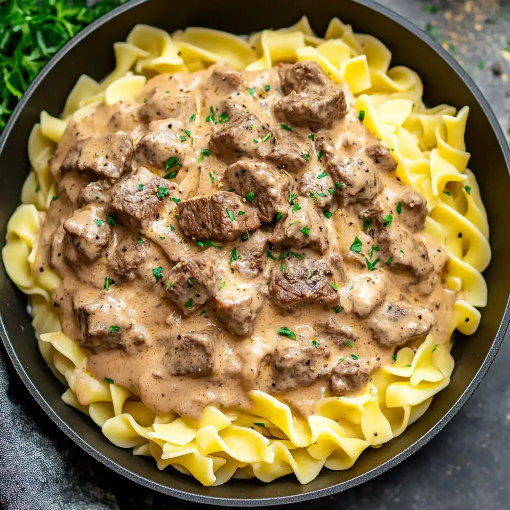 Creamy beef stroganoff served over tender egg noodles, garnished with parsley.